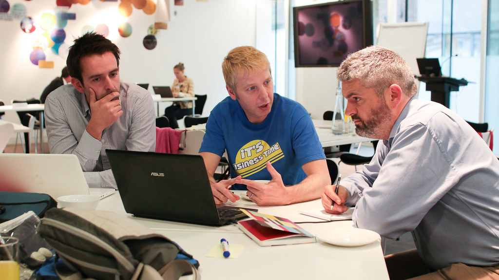 Three men discussing work around a laptop in an open office